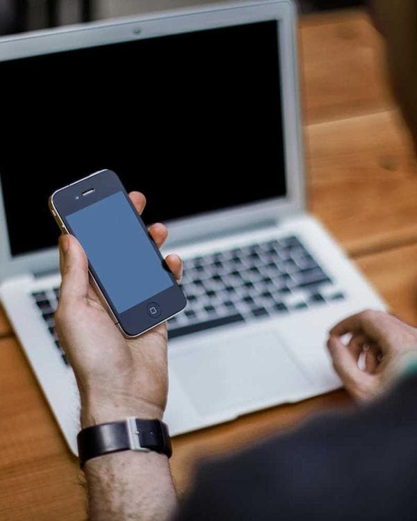 Hands holding a phone over a laptop